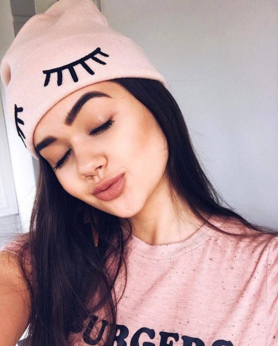 Chica con los ojos cerrados, inclinando su cabeza con gorro rosa pastel