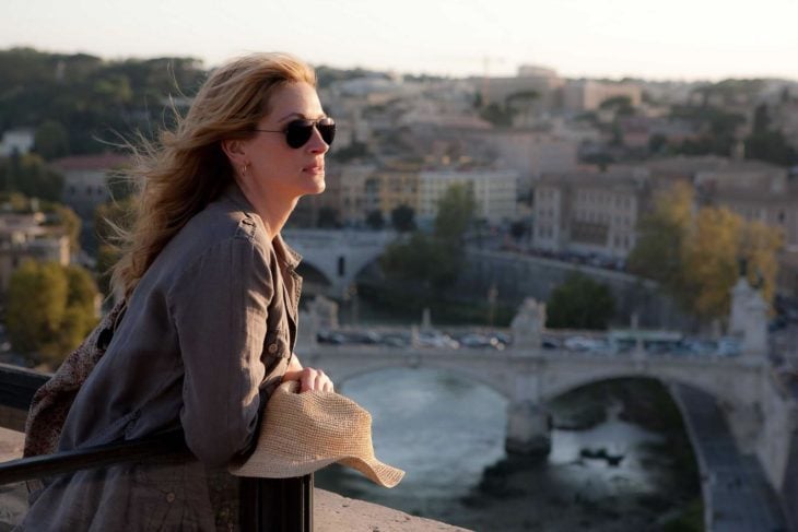 una mujer con lentes sobre un puente ve una ciudad a lo lejos