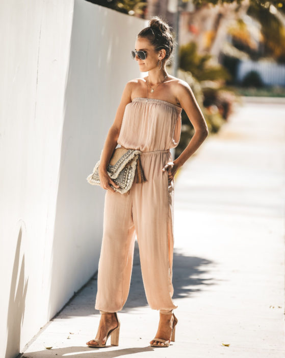 Looks con jumpsuit; mujer peonada con un bun alto, vestida con un enterizo color beige sin hombros y zapatillas de tacones gruesos