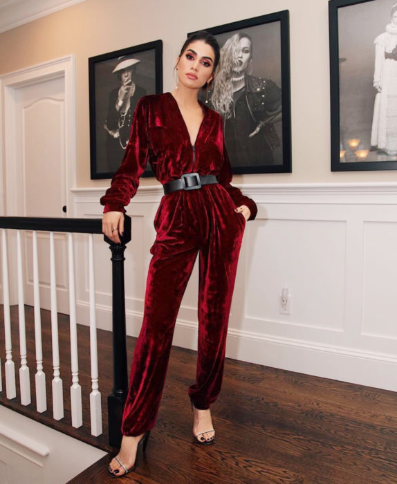 Looks con jumpsuit; mujer frente a retratos en blanco y negro, posando al lado de escaleras con un enterizo rojo de terciopelo con sandalias stiletto