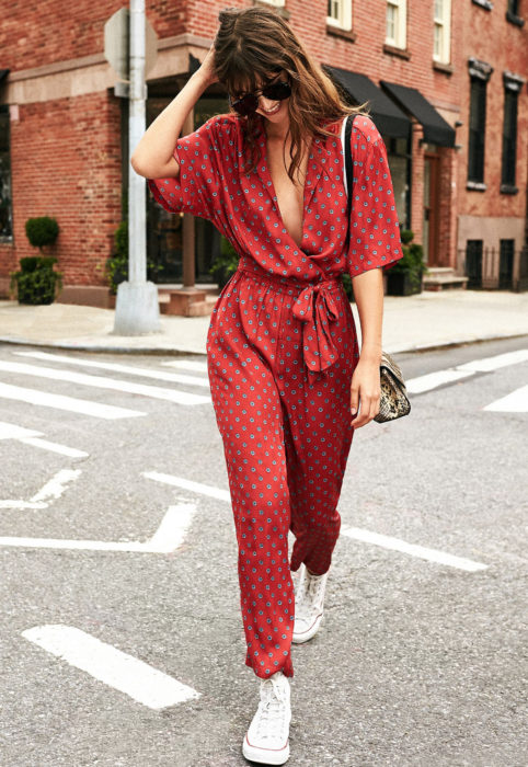 Looks con jumpsuit; chica de cabello castaño, suelto despeinado, con lentes de sol, un enterizo color rojo de mangas cortas holgadas y tenis converse blancos