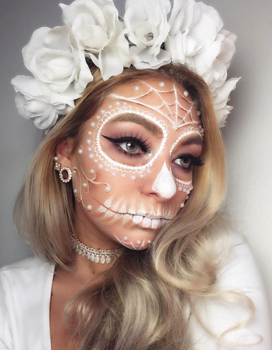 Maquillaje moderno blanco de Catrina de Día de Muertos; chica rubia con corona de rosas blancas en la cabeza