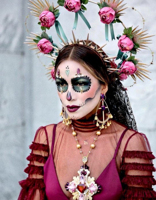 Maquillaje moderno de Catrina de Día de Muertos, con diadema dorada de picos y corona de estrellas y flores rosas, maxicollar y aretes de cruz