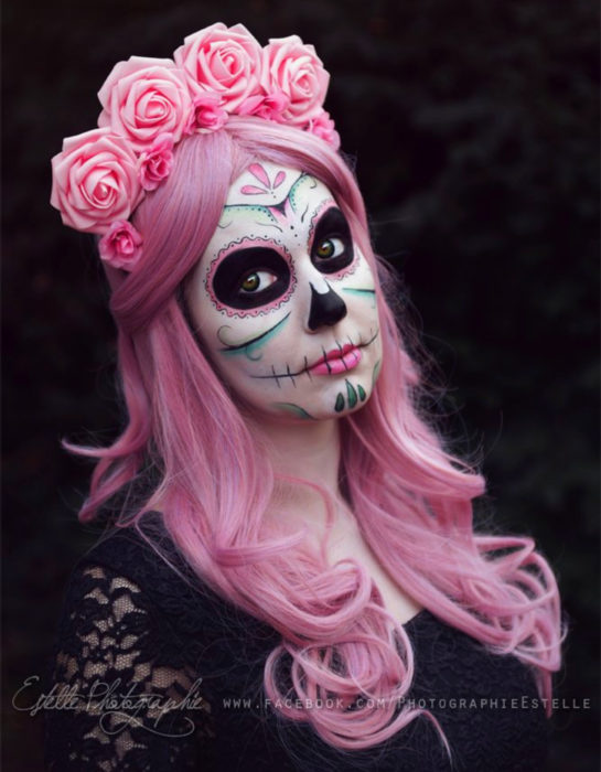 Maquillaje moderno de Catrina de Día de Muertos; chica de cabello largo, ondulado y rosa, corona de flores y blusa de encaje negro