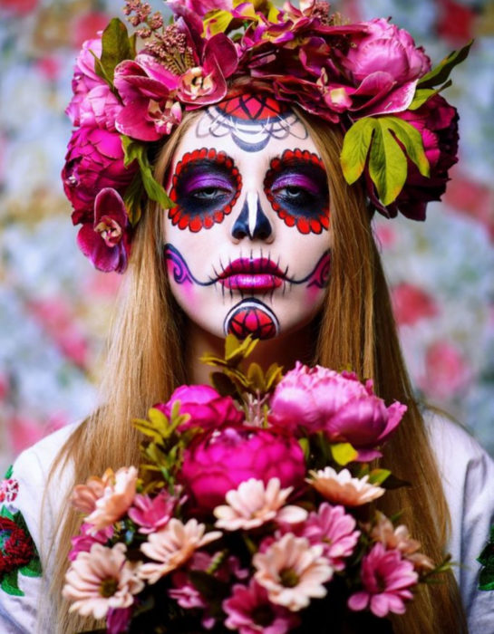 Maquillaje tradicional de Catrina de Día de Muertos color rojo y rosa con corona de flores en le cabeza y ramo