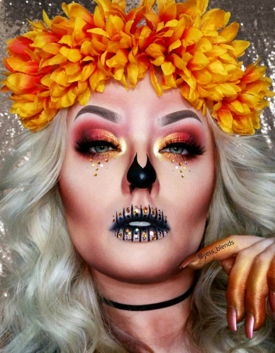 Maquillaje moderno de Catrina de Día de Muertos con flores de cempasúchil en el cabello, ojos con sombras anaranjadas y lentejuelas