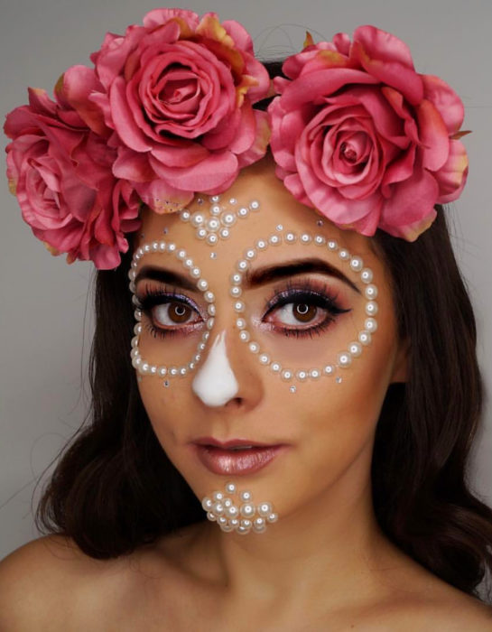 Maquillaje moderno de Catrina de Día de Muertos con corona de rosas en la cabeza y adornos de perlas blancas