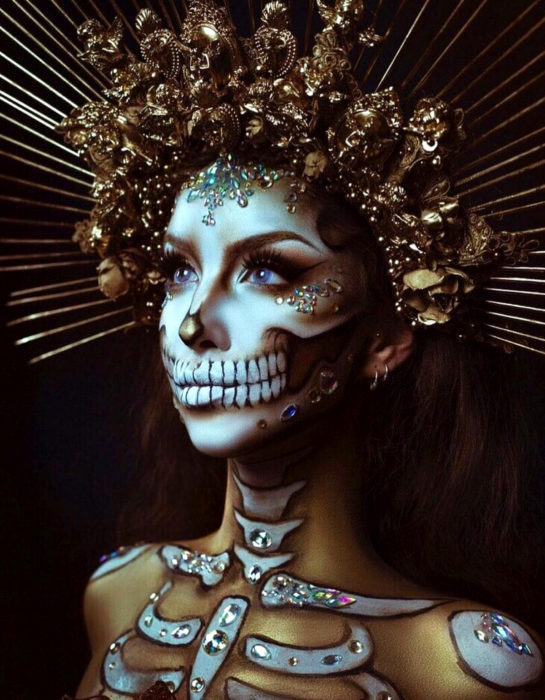 Maquillajemoderno de Catrina de Día de Muertos; mujer de ojos azules con corona dorada y piedras swarovski en el rostro