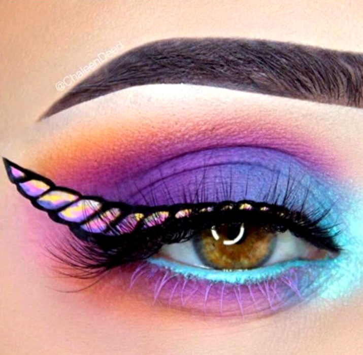 Maquillaje de ojos de Halloween; sombra morada, azul y rosa, con delineado cat eye de cuerno de unicornio 