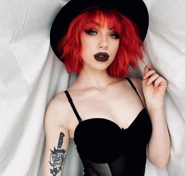 Chica usando corset negro, con sombrero oscuro, cabello rojo