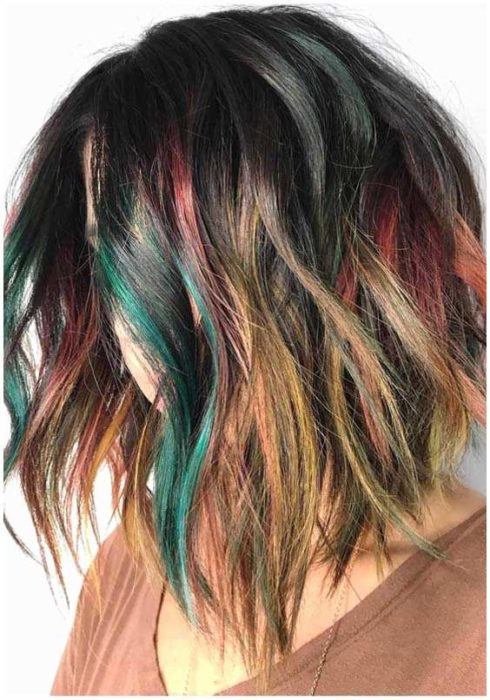 Chica de perfil mostrando su cabello con mechas de colores verde, vino y amarillo