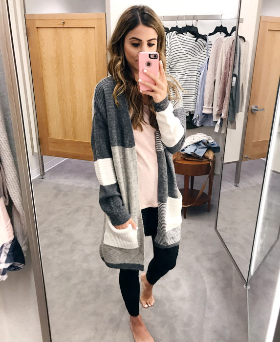 Oversized cardigan; mujer tomándose una selfie frente al espejo, con suéter holgado color gris y blanco