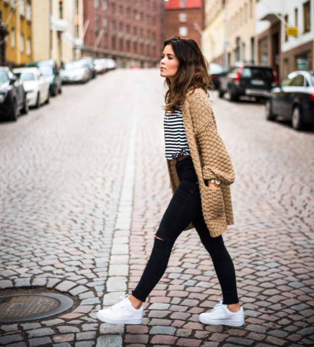 Oversized cardigan; chica caminando en calle empedrada con suéter holgado tejido color café, con pantalones entubados y tenis blancos