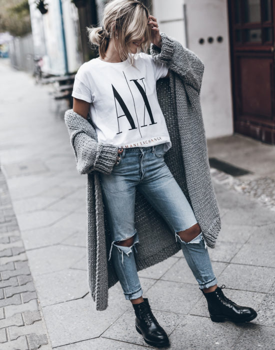 Oversized cardigan; mujer rubia con coleta despeinada, con playera de Armani, con pantalones rasgados, botas militares y suéter holgado tejido color gris, en la calle