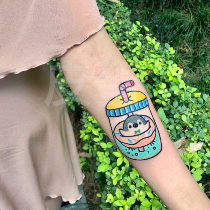 Tatuajes tiernos de Pikka Cool Cool Tattoo; tatuaje kawaii de pinguino sobre una dona en un termo con agua