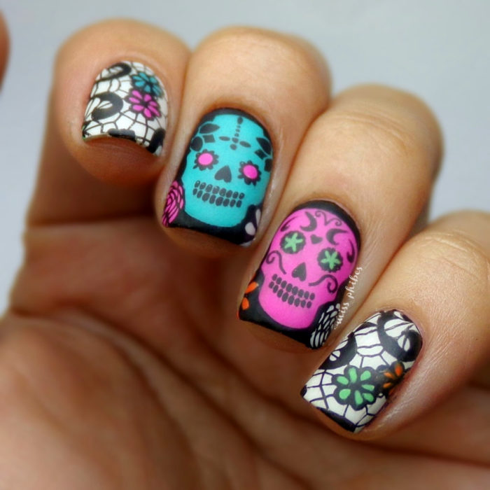 Manicura de Día de Muertos; uñas cortas cuadradas pintadas de negro con diseño de calaveras y flores de papel picado