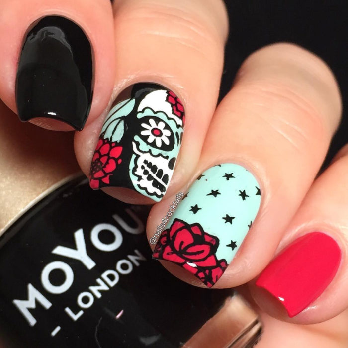 Manicura de Día de Muertos; uñas largas cuadradas pintadas con esmalte negro, azul y rojo con diseño de calaveras de dulce con flores