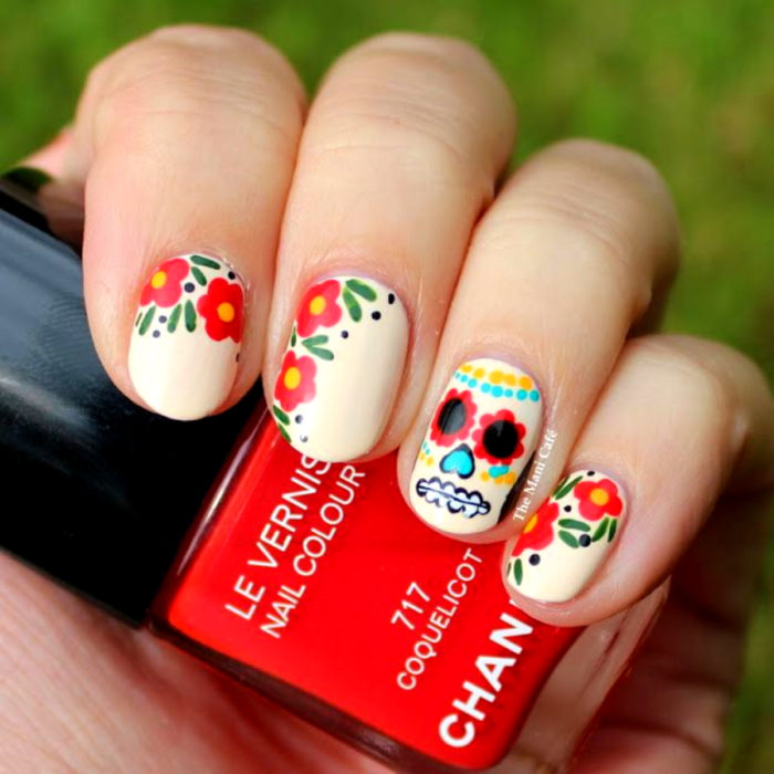 Manicura de Día de Muertos; uñas cortas pintadas con esmalte blanco con calavera de dulce y flores rojas