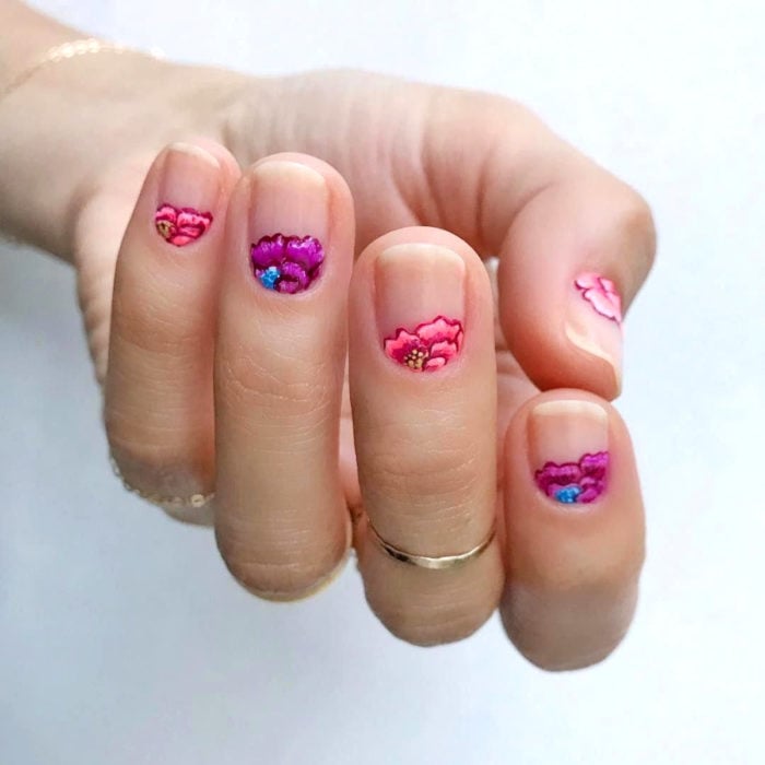 Manicura de Día de Muertos; uñas cortas pintadas con esmalte transparente y flores de altar de color rosa y morado