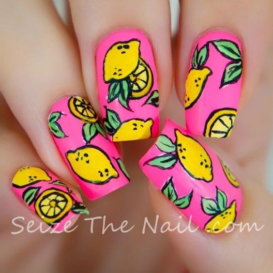 Manos de una chica con diseño de uñas pop art con estampados de limones y el fondo de color rosa 