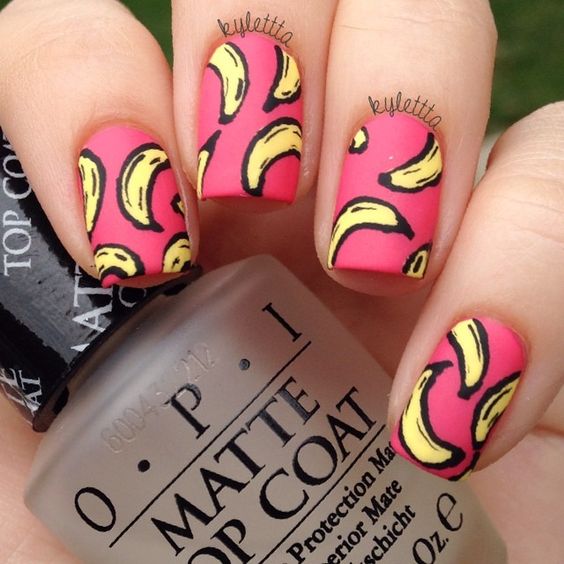 Manos de una chica con diseño de uñas pop art en color rosa con plátanos dibujados 