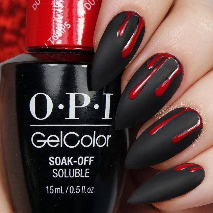 Chica con unas uñas en forma de almendra y de color negro con diseños estilo sangre de color rojo 