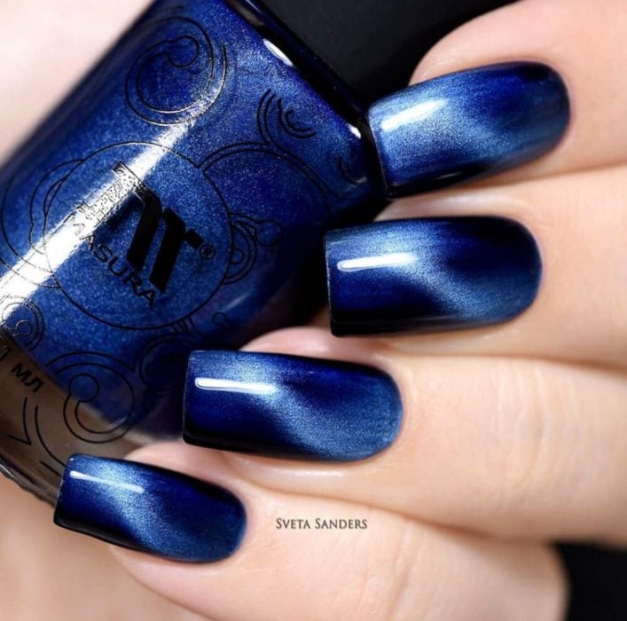 Chica mostrando las uñas azul cobalto mientras sostiene un esmalte 