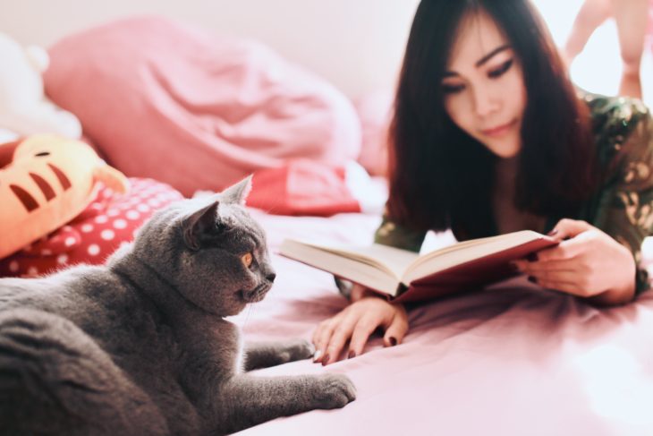 Mujer leyendo un libro y su gato junto a ella