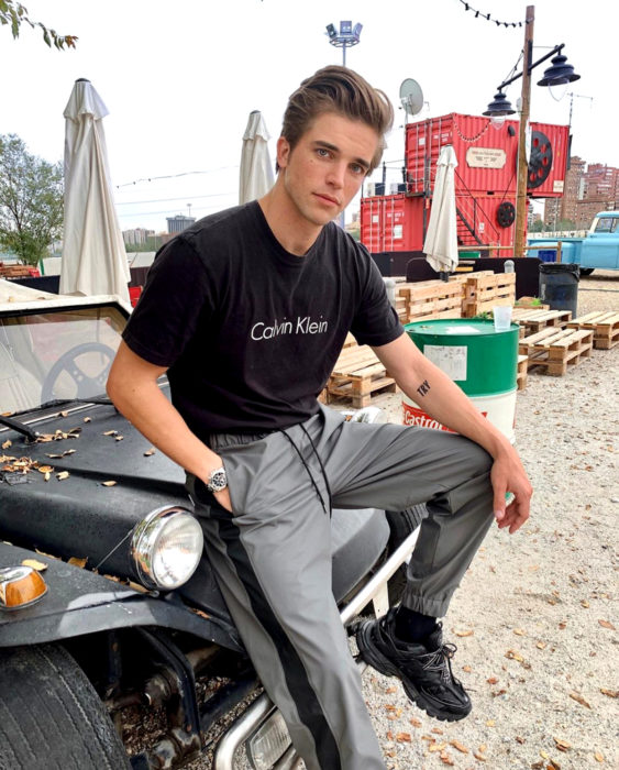 Finlandia te paga por tener bebés; guapo chico finlandés sentado en un Jeep, con playera de Calvin Klein, pants grises y tenis Fila