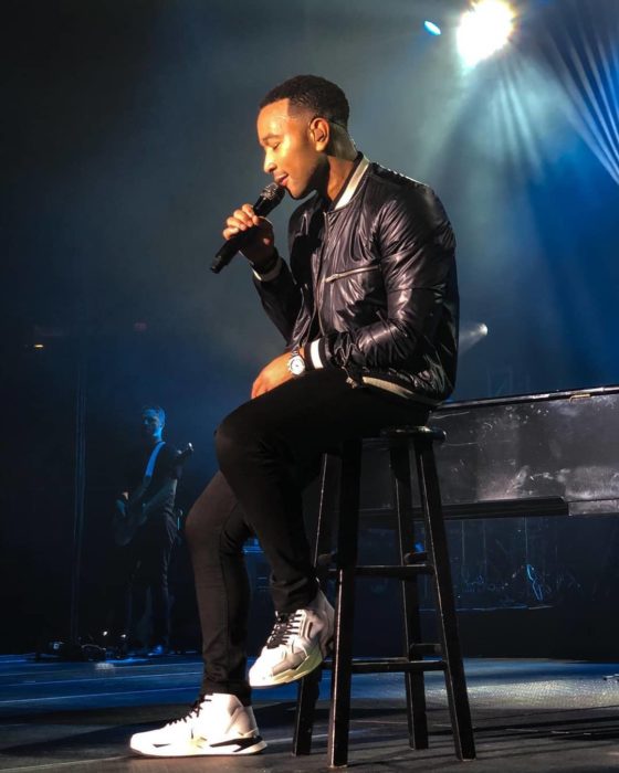 John Legend cantando en un concierto mientras está sentado en un banco