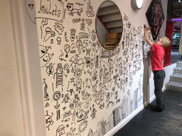 Niño dibujando la pared de un restaurante con diferentes dibujos 