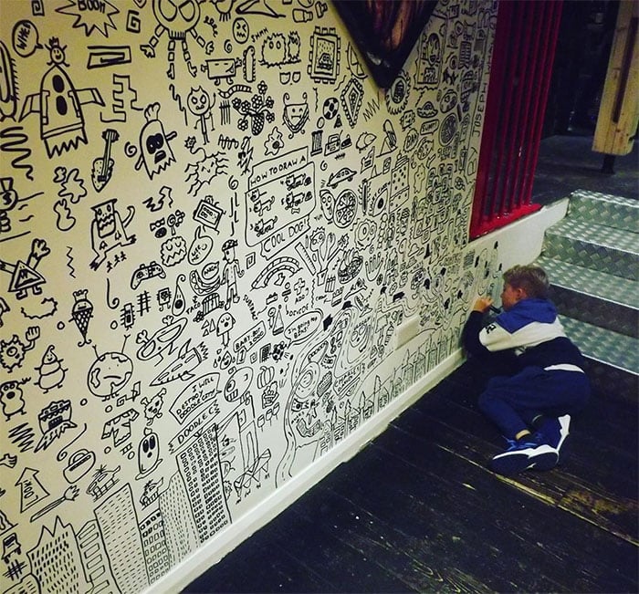 Niño dibujando la pared de un restaurante con diferentes garabatos 