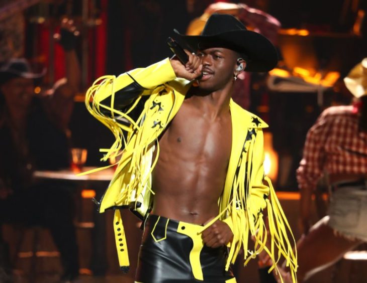 Cantante Lil Nas X usando una chaqueta de color amarillo con un sombrero negro y jeans 