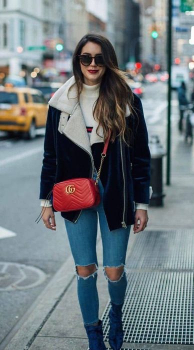 Chica caminando por la calle mientras usa un atuendo de chaqueta negra con una chaqueta de color negro, jeans y bolsa cruzada sobre el pecho