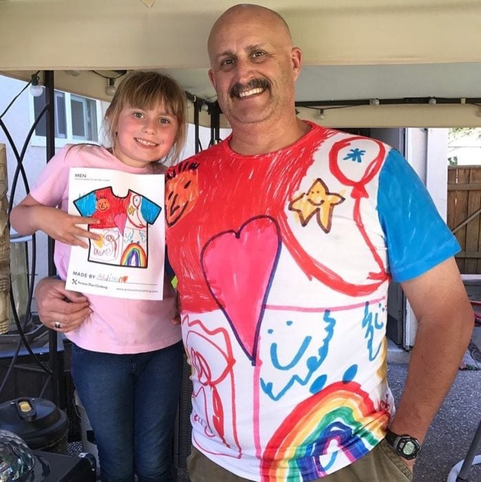 Ppá abrazando a su hija llevando una camisa con los dibujos que ella hizo