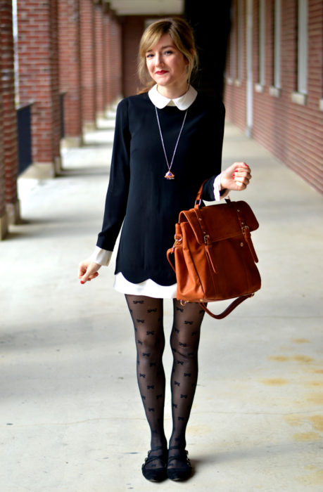 Chica vestida de Merlina Adams; vestido negro con cuello blanco, bolsa de mano café, medias de moños y flats