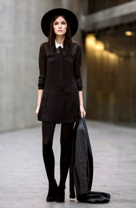 Chica de cabello lacio y mediano, con sombrero, vestido, medias y botines negros, con abrigo fris