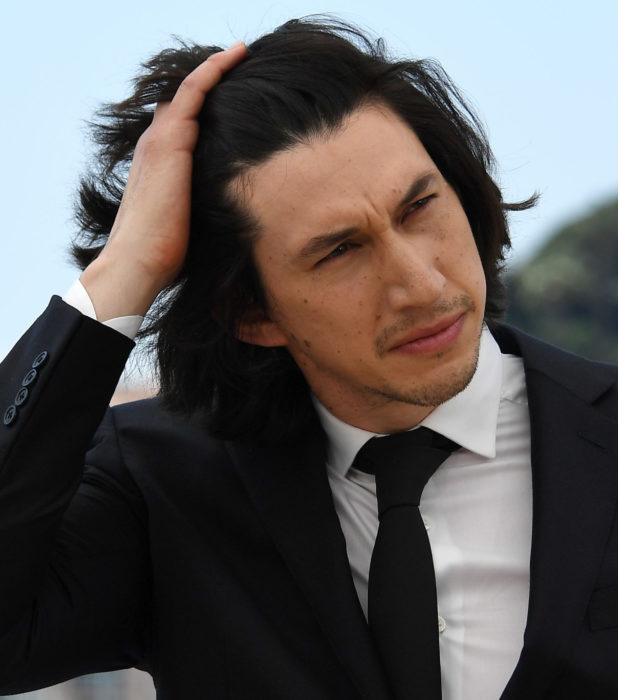 Actor Adam Driver; hombre de traje y corbata, acomodándose el cabello negro y largo