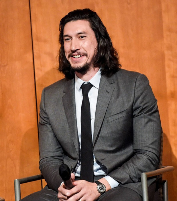 Actor Adam Driver; hombre sentado con micrófono en mano, cabello largo y negro, barba y bigote