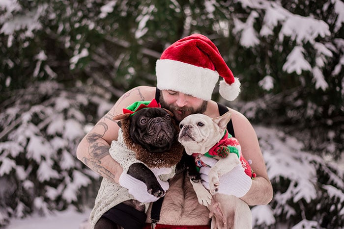 Hombre vestido de santaclaus cargando a dos perritos mientras posan para la sesión de fotos de un calendario