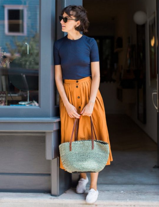 Pantone elije el classic blue como el color del 2020; mujer de cabello corto con blusa azul clásico, falda midi anaranjada y bolsa tejida 