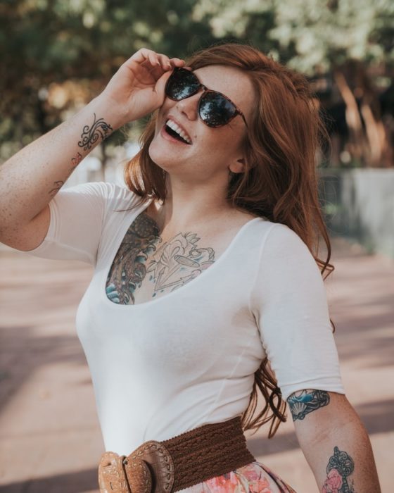 Ragazza con tatuaggi sorridenti e con gli occhiali scuri 