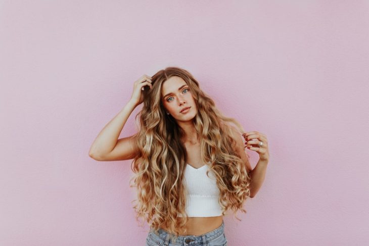 Ragazza con i capelli lunghi, biondi e ricci carichi su una parete rosa pastello