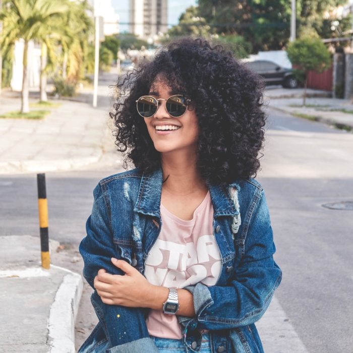 Ragazza dei capelli ricci con giacca di jeans che cammina per strada e sorridente