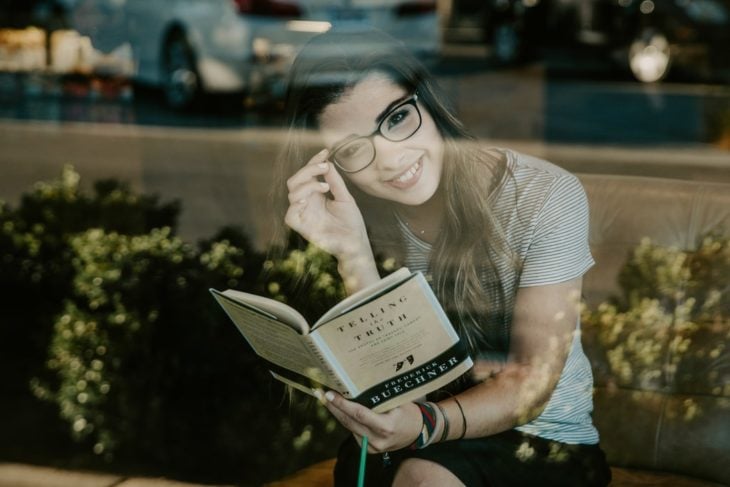 Chica leyendo un libro dentro de una cafetería y sonriendo 