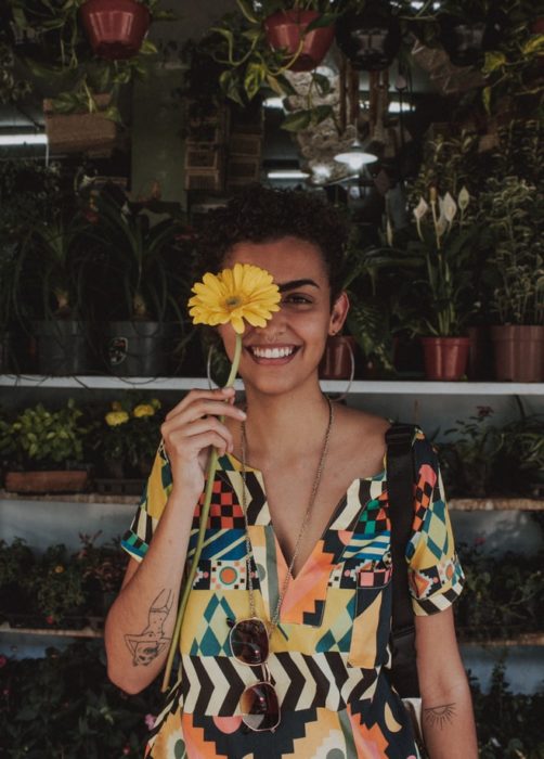 Chica sosteniendo un girasol en su mano y cubriendo su rostro