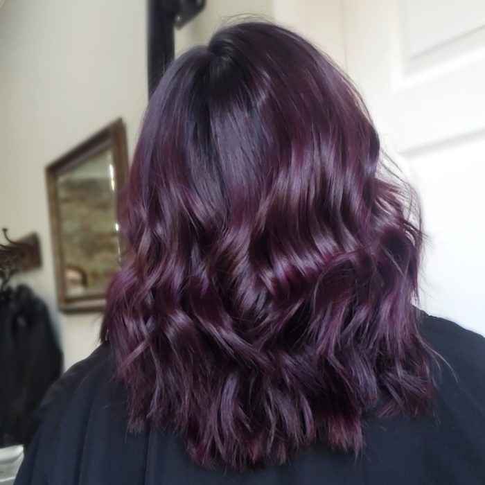 Chica mostrando su cabello de color dark violeta con destellos que brillan en la luz 