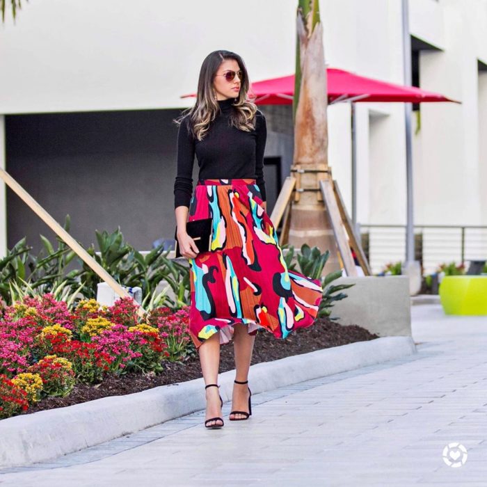 chica con blusa negra y falda plisada en tonos rojos