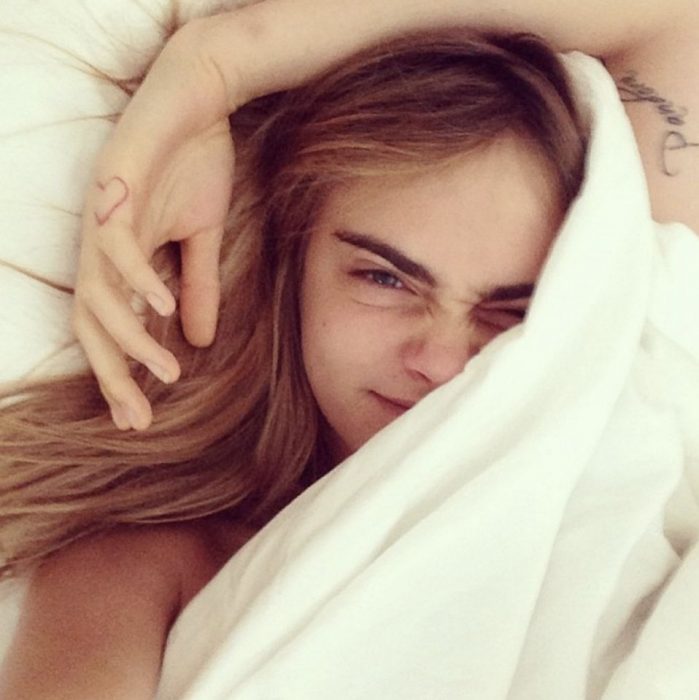 Cara Delevingne sin maquillaje, recostada en su cama, cubriendo su rostro con una sabana blanca