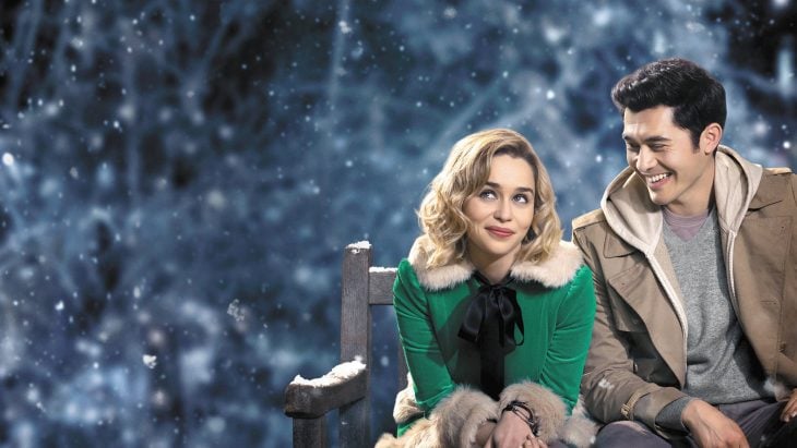 Emilia Clarke y Henry Golding sentados en una banca mientras actuan en la película Last Christmas 